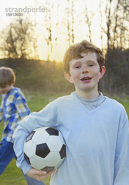 Portrait Junge mit Sommersprossen hält Fußball im Park