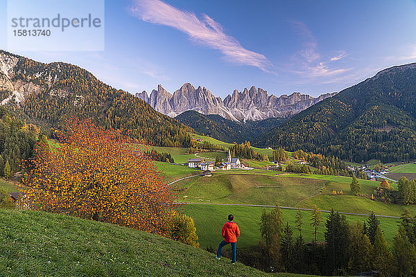 Rückansicht eines Mannes  der die Geislerspitzen und das kleine Dorf Santa Magdalena im Herbst bewundert  Funes  Dolomiten  Südtirol  Italien  Europa