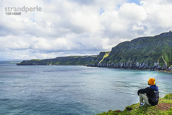 Ein junger Wanderer macht eine Pause auf einem Wanderweg entlang der Antrim-Küste  Ulster  Nordirland  Vereinigtes Königreich  Europa