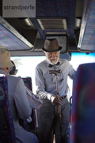 Aktiver älterer Mann mit Hut und Gehstock beim Einsteigen in einen Reisebus
