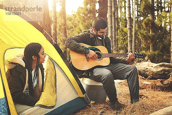 Junges Paar spielt Gitarre im Zelt auf einem Campingplatz im Wald