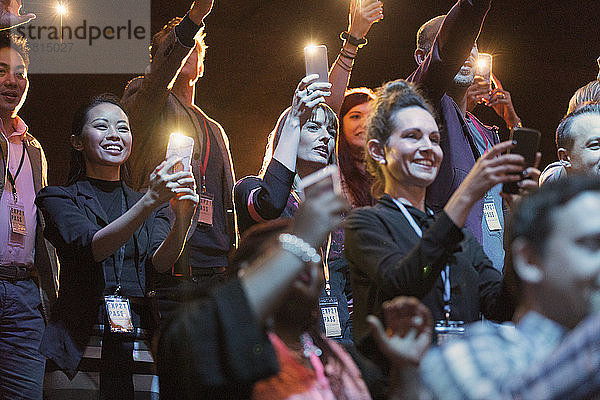 Lächelndes Publikum mit Fotohandy-Taschenlampen im dunklen Hörsaal