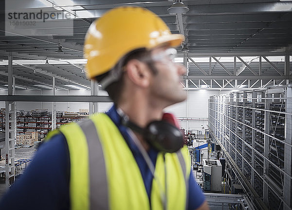 Männlicher Arbeiter  der auf einer Plattform in einer Fabrik wegschaut