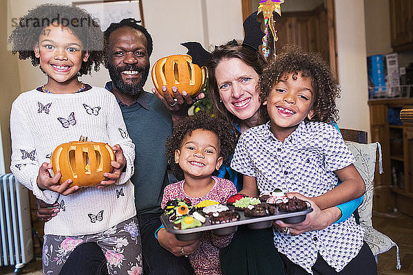 Porträt einer glücklichen Familie mit geschnitzten Kürbissen und Halloween-Cupcakes