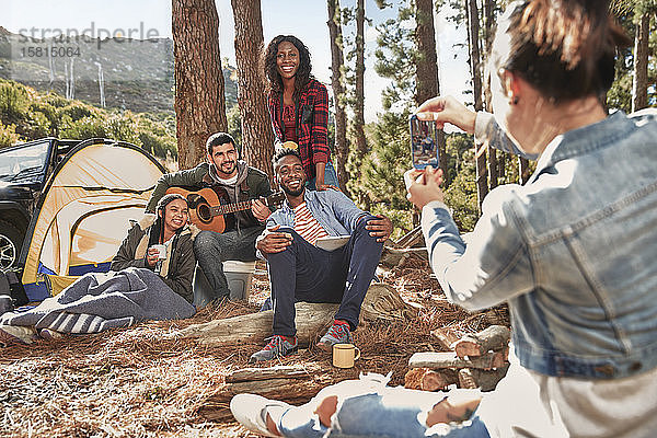 Junge Frau mit Fotohandy  die ihre Freunde auf einem Campingplatz im Wald fotografiert