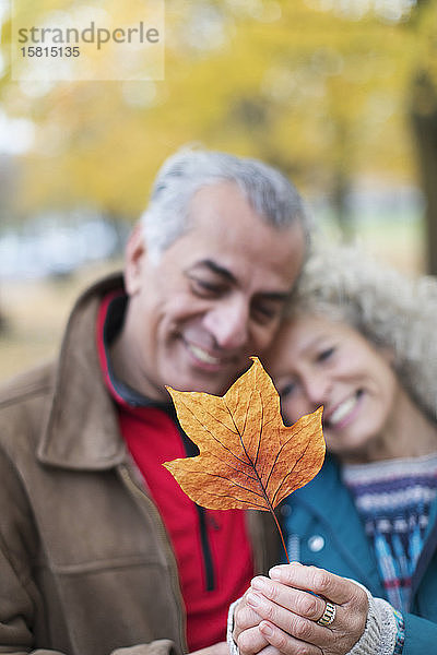 Zärtliches älteres Paar hält orangefarbenes Herbstblatt