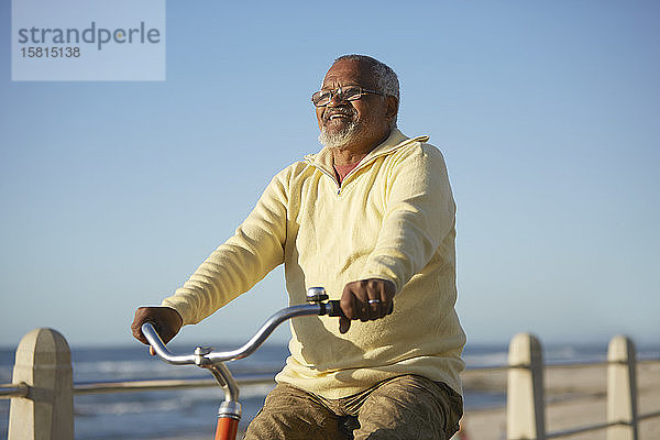 Sorgloser aktiver älterer Mann  der mit dem Fahrrad am Meer entlang fährt