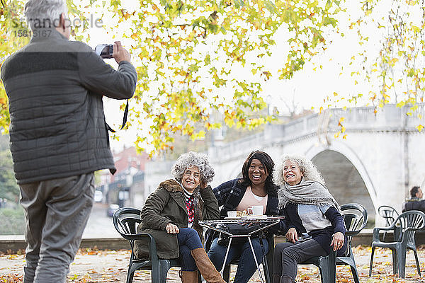 Älterer Mann fotografiert aktive ältere Freundinnen im Herbstparkcafé