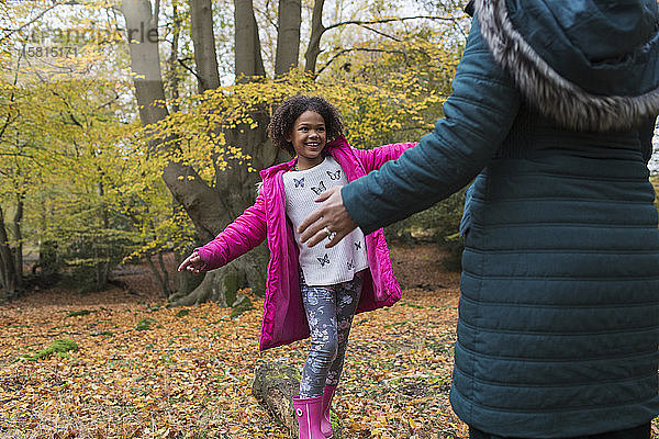 Glückliche Mutter und Tochter spielen auf einem umgestürzten Baumstamm im Herbstwald