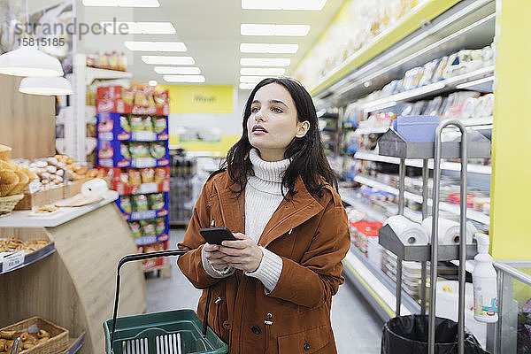 Frau mit Smartphone beim Einkaufen im Supermarkt