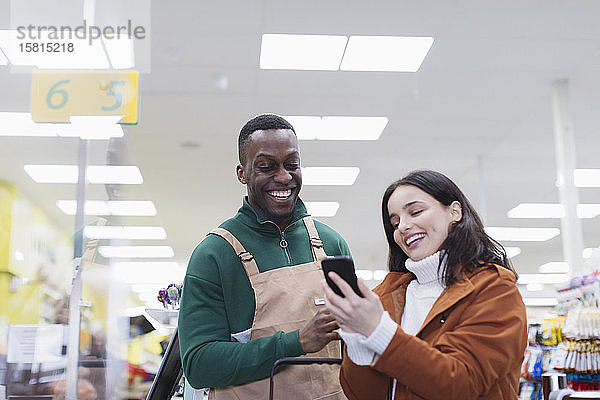 Lebensmittelhändlerin hilft Kunden mit Smartphone im Supermarkt