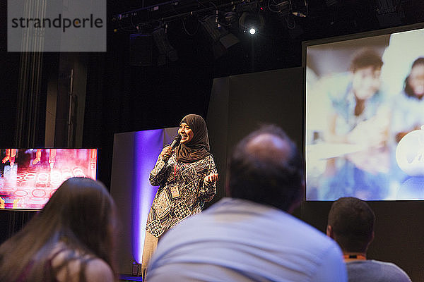 Lächelnde Rednerin im Hidschab im Gespräch mit Mikrofon auf der Bühne