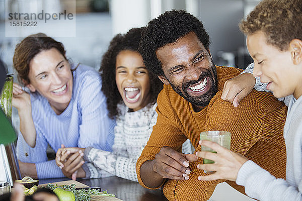 Lachende Familie beim Trinken eines gesunden grünen Smoothies in der Küche