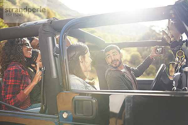 Mann mit Digitalkamera macht Selfie im Jeep mit Freunden