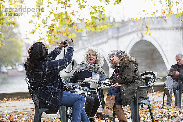 Frau mit Digitalkamera beim Fotografieren aktiver älterer Freundinnen im Herbstparkcafé