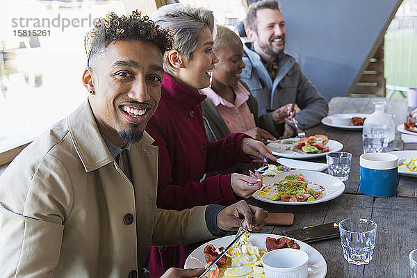 Porträt lächelnder junger Mann beim Frühstück mit Freunden in einem Restaurant im Innenhof