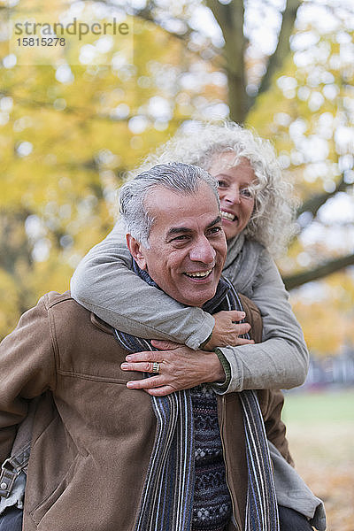 Verspieltes  lächelndes älteres Paar nimmt im Herbst im Park Huckepack