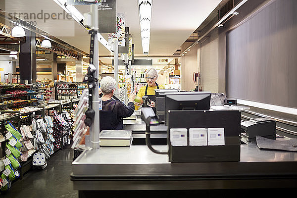 Ältere weibliche Kassiererin hilft Kunden an der Supermarktkasse