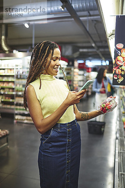 Lächelnde Frau mit Smartphone beim Lebensmitteleinkauf im Supermarkt