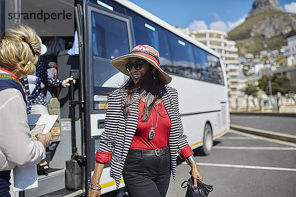 Lächelnde aktive ältere Touristin beim Aussteigen aus dem Reisebus