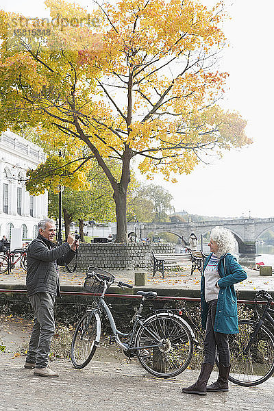 Älterer Mann fotografiert Frau mit Fahrrad in herbstlicher Stadt