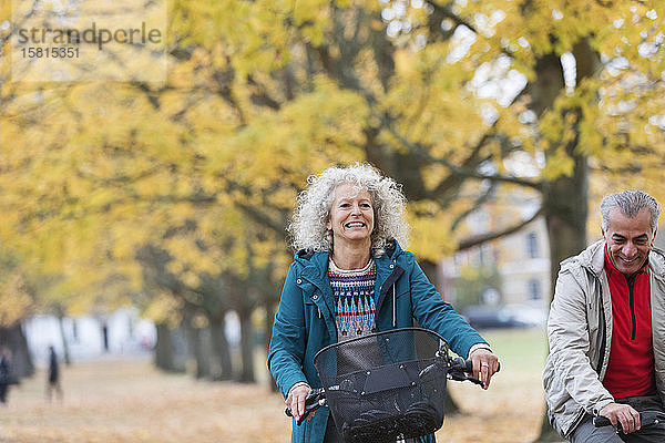 Lächelnde  unbekümmerte ältere Frau auf dem Fahrrad zwischen Bäumen im Herbstpark