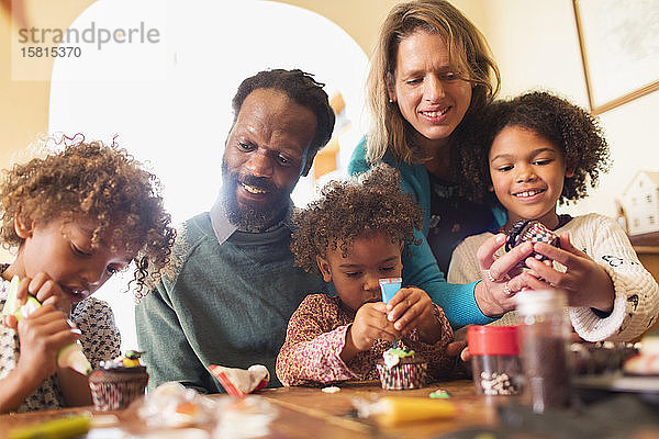 Multiethnische Familie beim Verzieren von Cupcakes am Tisch