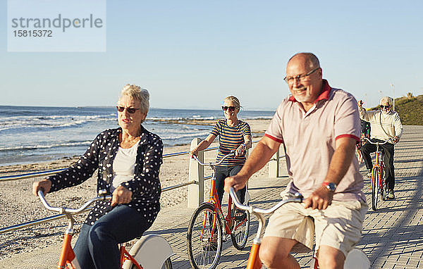 Aktive ältere Touristenfreunde beim Radfahren auf der sonnigen Strandpromenade am Meer