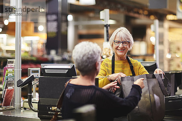 Freundliche ältere weibliche Kassiererin hilft Kunden an der Supermarktkasse