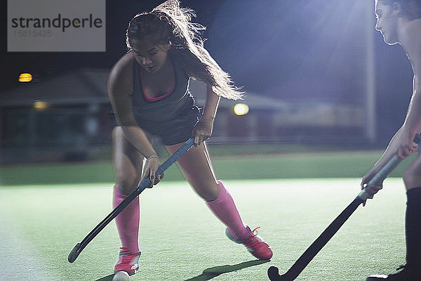 Entschlossene junge Feldhockeyspielerin mit Hockeyschläger  die nachts auf dem Feld spielt