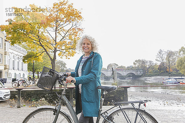 Porträt lächelnd ältere Frau Fahrradfahren entlang Herbst Fluss