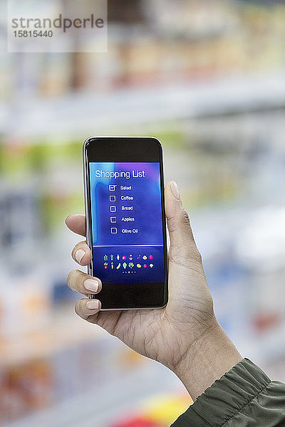 Persönliche Perspektive einer Frau  die im Supermarkt auf eine digitale Einkaufsliste auf ihrem Smartphone schaut