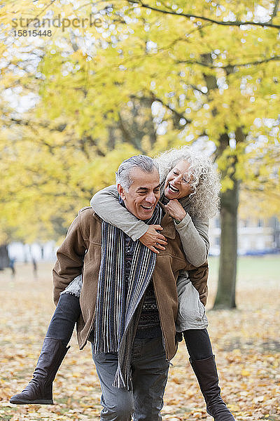 Verspieltes älteres Paar nimmt im Herbst Huckepack im Park