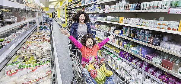 Mutter schiebt verspielte Tochter im Einkaufswagen im Supermarktgang