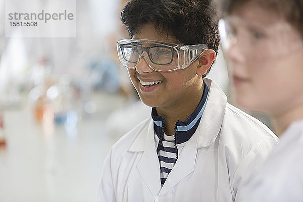 Lächelnder Junge mit Schutzbrille und Laborkittel in einem Laborklassenzimmer