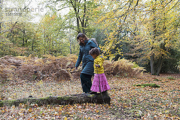 Mutter und Tochter gehen auf einem umgestürzten Baumstamm im Herbstwald spazieren