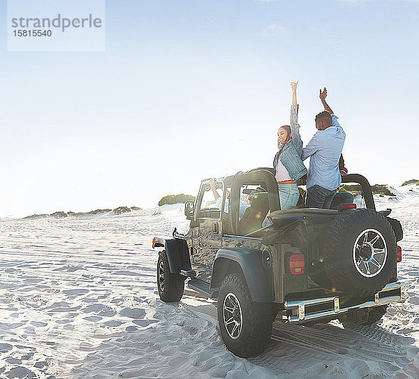 Enthusiastische junge Freunde mit erhobenen Armen  die einen Road Trip am sonnigen Strand genießen