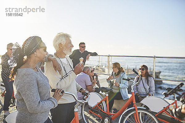 Aktive Seniorenfreunde mit Fahrrädern essen Eis am sonnigen Meer