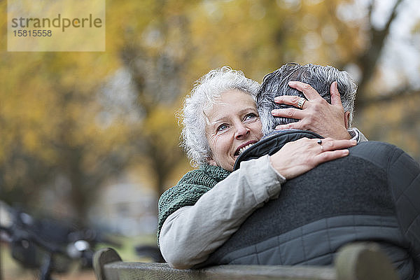 Lächelndes  zärtliches älteres Paar  das sich auf einer Bank im Herbstpark umarmt