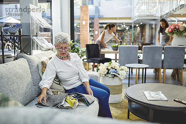 Ältere Frau betrachtet Stoffmuster auf einem Sofa in einem Einrichtungsgeschäft