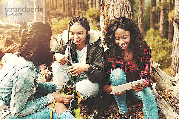Junge Freundinnen trinken Kaffee und benutzen ein digitales Tablet im Wald