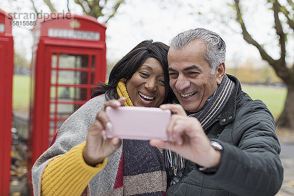 Lächelndes älteres Paar macht ein Selfie im Park vor einer roten Telefonzelle