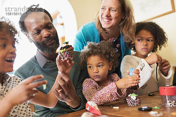 Glückliche multiethnische Familie beim Verzieren von Törtchen am Tisch