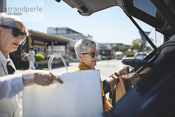 Ältere Frauen laden auf einem sonnigen Parkplatz Einkaufstüten in den Kofferraum eines Autos