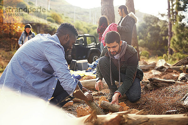 Junge Männer und Freunde bauen ein Lagerfeuer auf einem Campingplatz