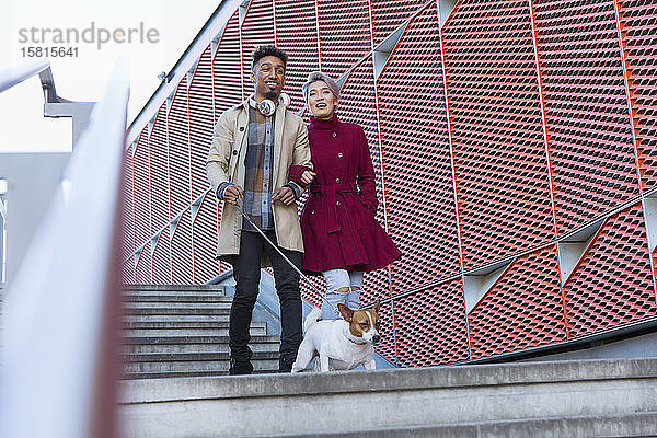 Lächelndes junges Paar  das mit seinem Hund eine moderne Stadttreppe hinuntergeht