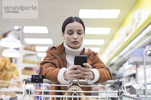 Junge Frau mit Smartphone beim Einkaufen im Lebensmittelladen