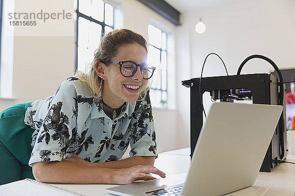 Lächelnde Designerin bei der Arbeit am Laptop neben dem 3D-Drucker im Büro