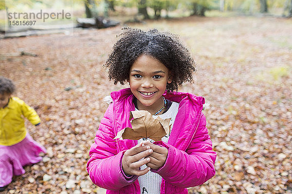 Porträt glückliches Mädchen hält Herbstblatt im Wald