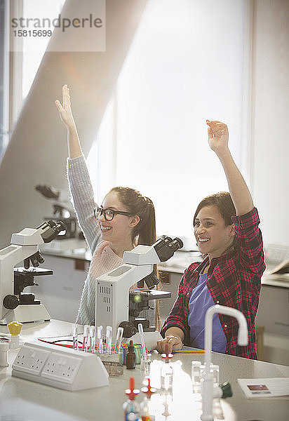 Eifrige Studentinnen heben die Arme hinter den Mikroskopen im Labor-Klassenzimmer